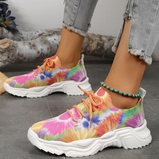 A pair of women's casual sports shoes with a multicolored floral pattern on the upper mesh and a white flat sole.