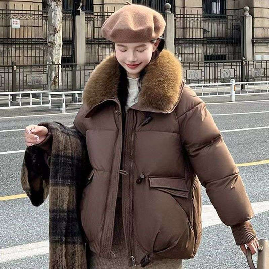 Person wearing a brown puffer jacket with fur collar on a street.