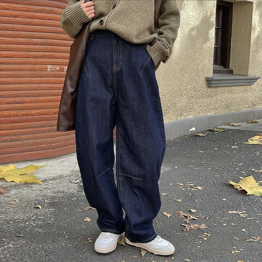 A person standing on the street wearing dark blue high-waisted wide-leg jeans and white sneakers.