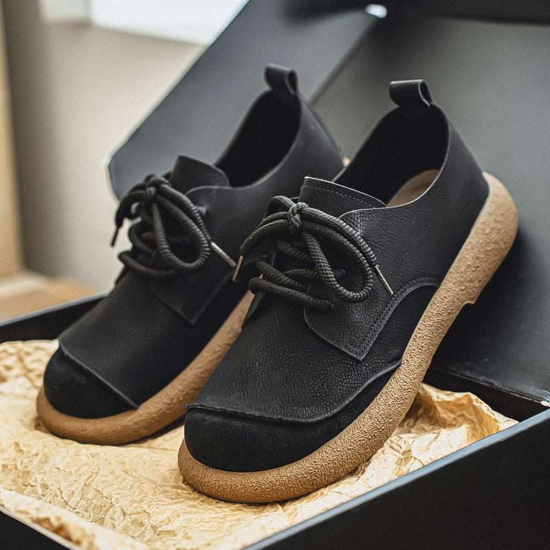 Black suede shoes with brown soles on a textured surface