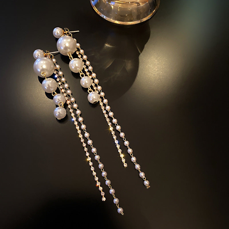 Pearl earrings with long chains on a dark surface