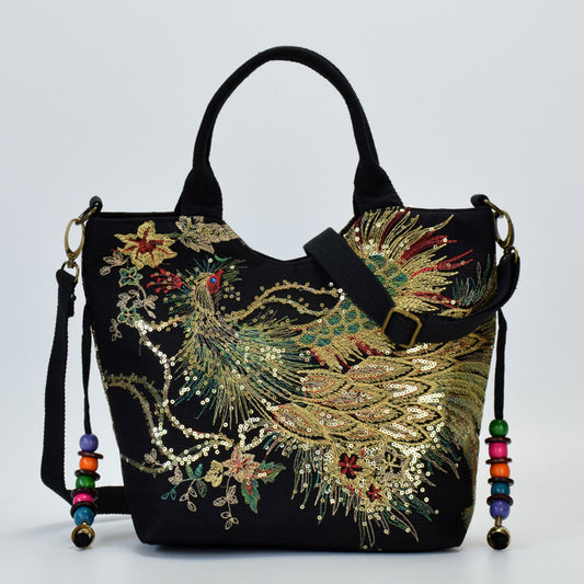 Black handbag with intricate gold embroidery and colorful tassels on a light gray background