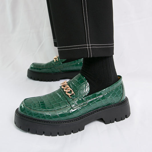 Green crocodile-patterned loafers with gold accents worn by a person on a white background