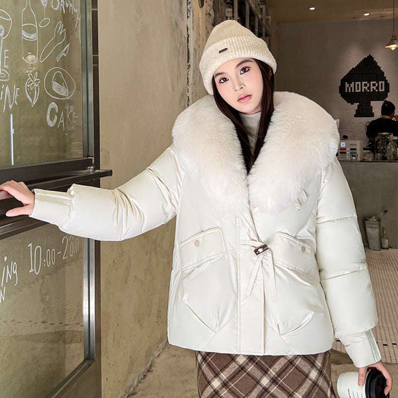 Woman wearing a white puffer jacket with a fur-lined hood in an indoor setting.