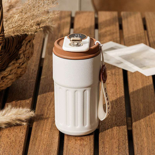 A white and brown smart digital thermal bottle with a stainless steel body and a digital display on the lid, placed on a wooden surface.