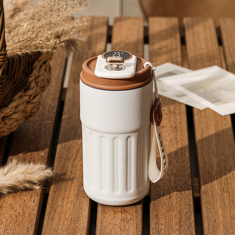 A white and brown smart digital thermal bottle with a stainless steel body and a digital display on the lid, placed on a wooden surface.