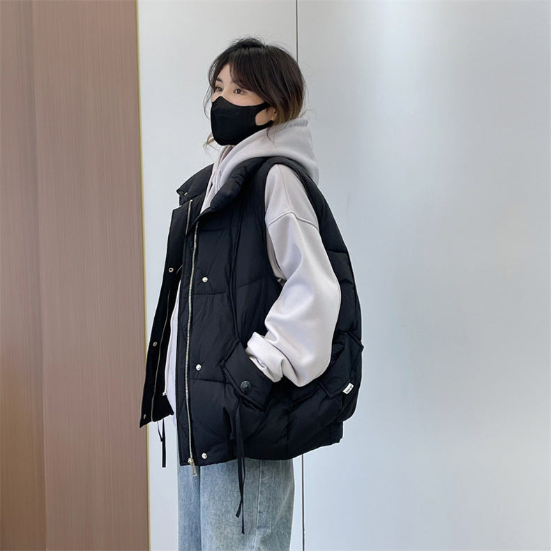 Person wearing a black puffer vest over a white hoodie against a neutral wall.