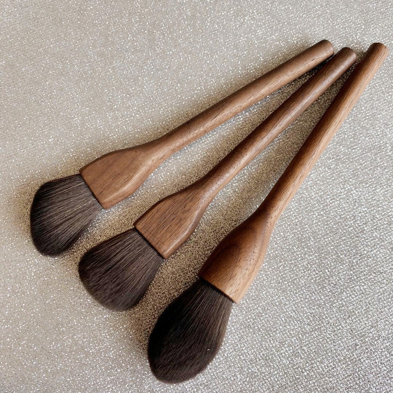 Set of four wooden makeup brushes with brown bristles on a textured beige background