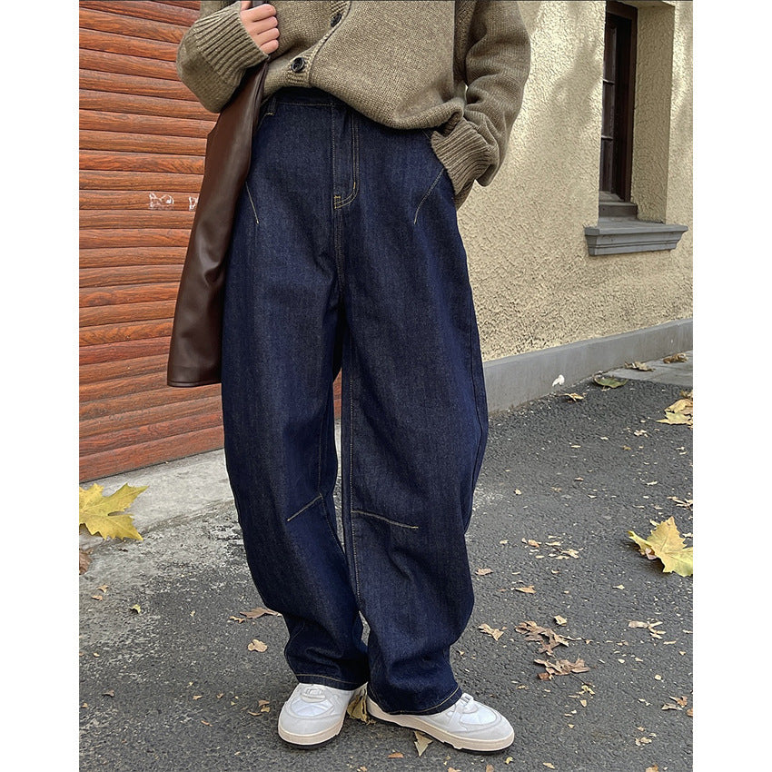 A person standing on the street wearing dark blue high-waisted wide-leg jeans and white sneakers.