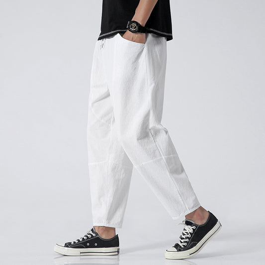 Person wearing white pants and black sneakers on a plain background