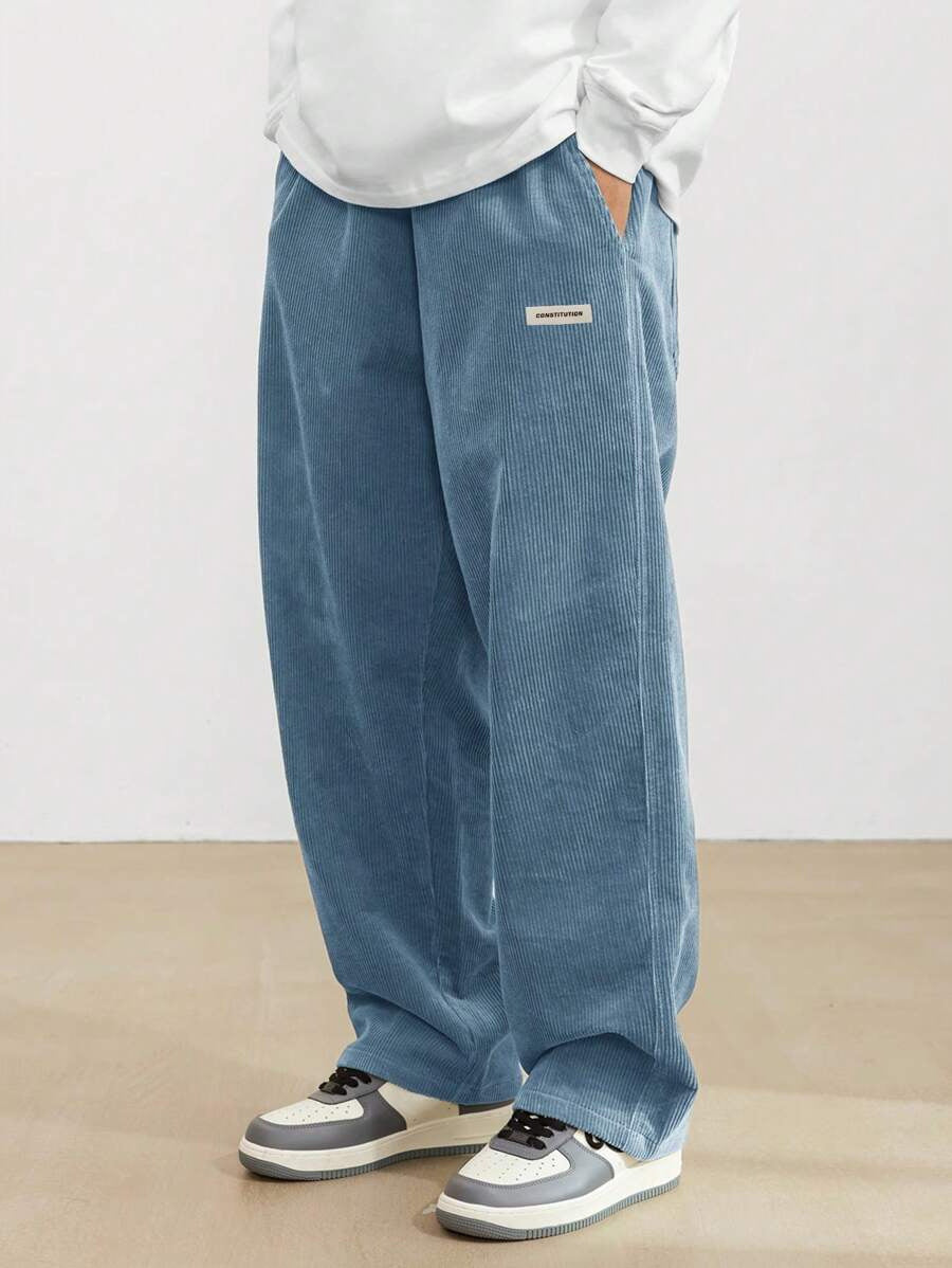 Person wearing blue corduroy pants with a white shirt and sneakers on a plain background