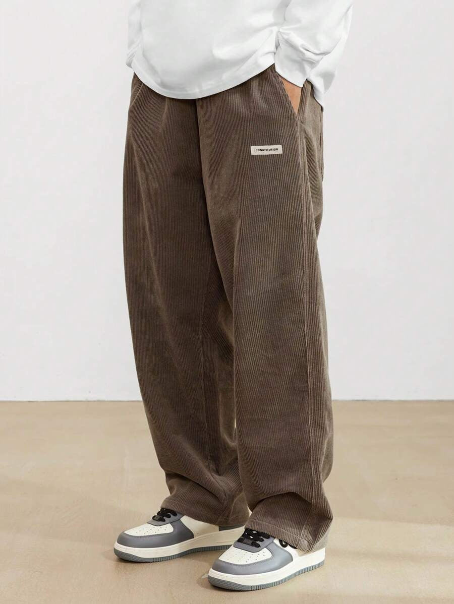Person wearing brown corduroy pants with a white shirt and gray sneakers on a plain background