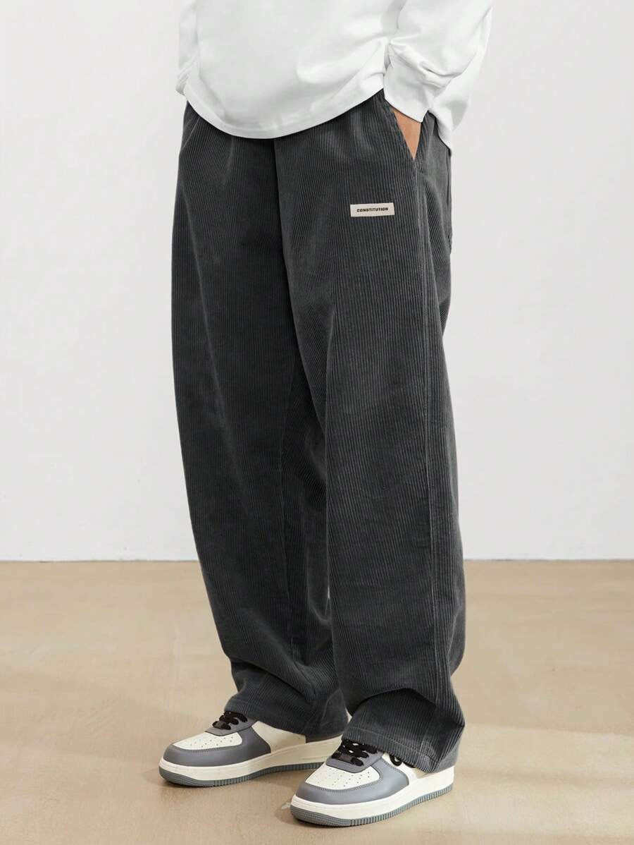 Person wearing dark gray wide-leg pants with a white shirt and sneakers on a plain background