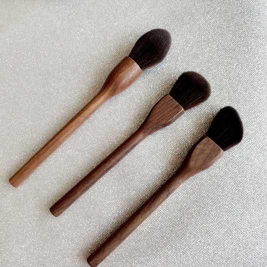Three wooden makeup brushes with black bristles on a textured beige background