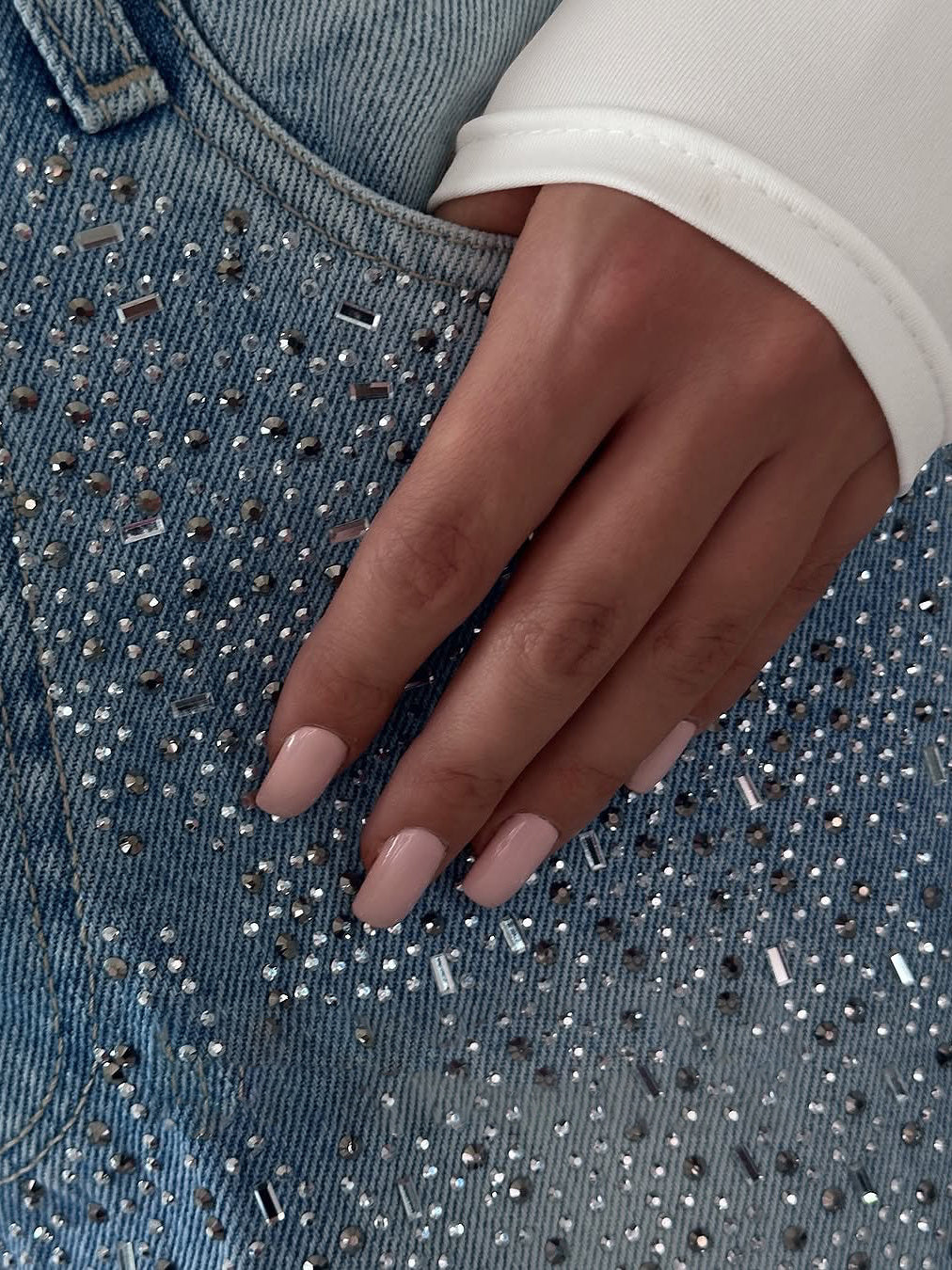 Close-up of a hand on a denim surface with rhinestones