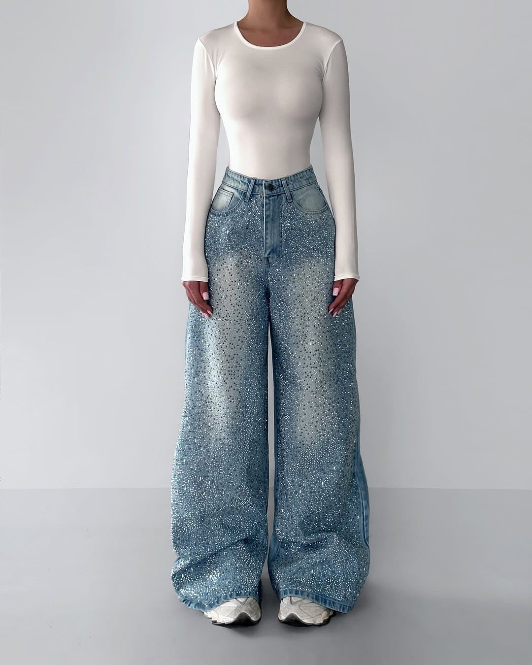 Person wearing a white long-sleeve top and blue wide-leg jeans on a gray background