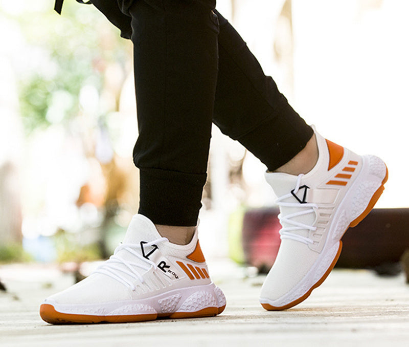 White sneakers with orange accents worn by a person on a blurred outdoor background