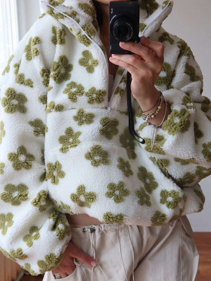 Person wearing a white sweater with green floral patterns, holding a camera.