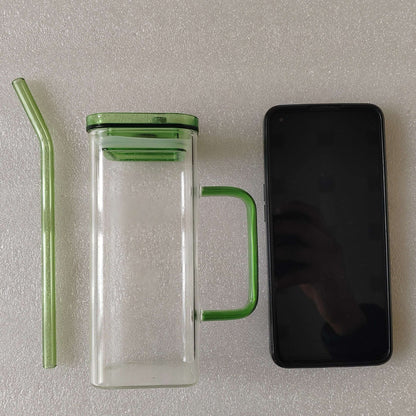 Square clear glass cup with green handle, straw, and sealed green-tinted lid.