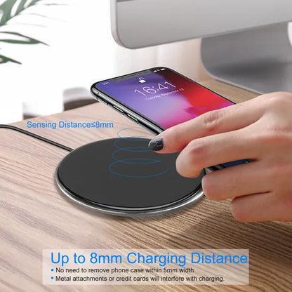 Black wireless charger pad on wood desk with smartphone placed on top