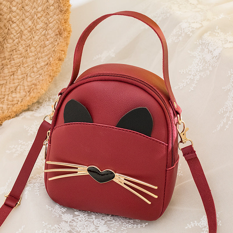 Red mini cat-face crossbody backpack with black ears, gold heart whisker bar, and strap