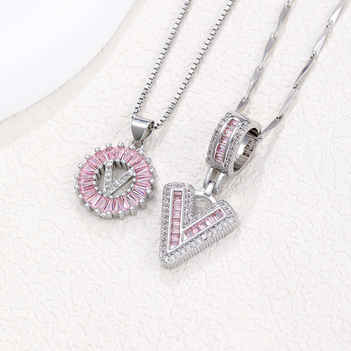 Silver-tone pendant necklace set with pink zircon rosette pendant and V-shaped block letter pendant.