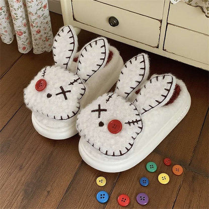 Pair of white bunny slippers with black details and red buttons on a wooden floor.