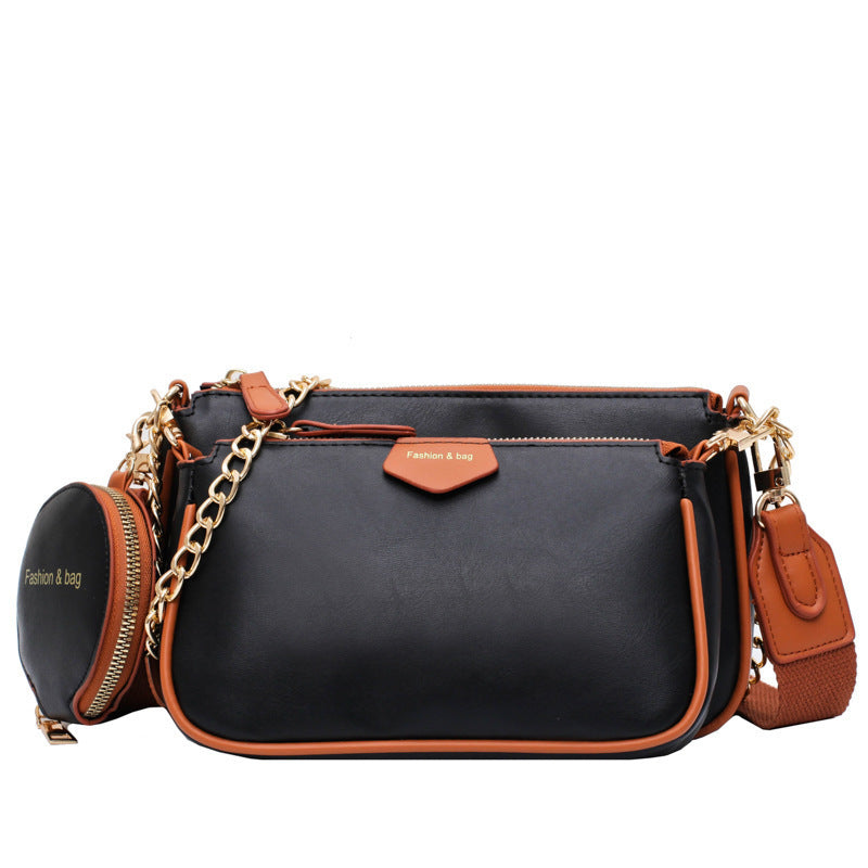 Black crossbody messenger bag with orange trim, gold chain strap, and round zip pouch.