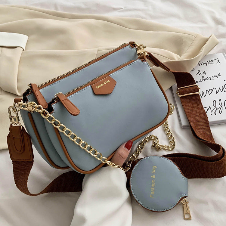 Light blue crossbody messenger bag with brown trim, gold chain strap, and round zip pouch.