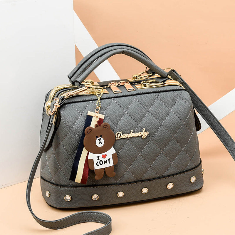 Dark blue quilted messenger bag with gold hardware, studded trim, bear keychain charm