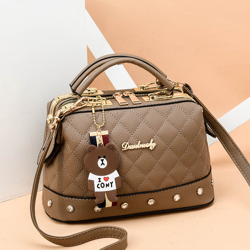 Khaki quilted messenger bag with gold hardware, studded base, bear keychain charm