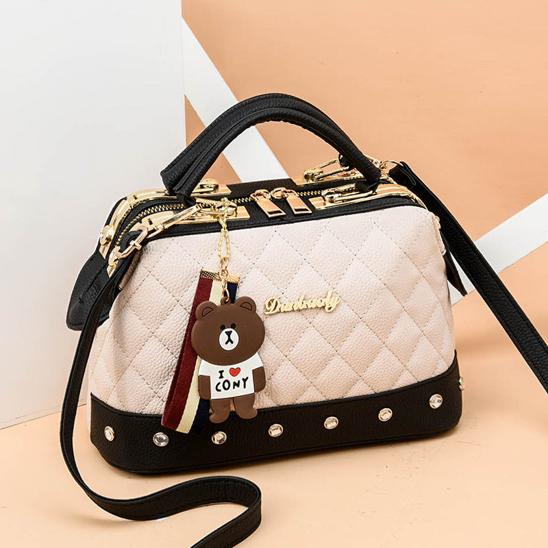 White quilted messenger bag with black trim, gold hardware, studded base, bear charm