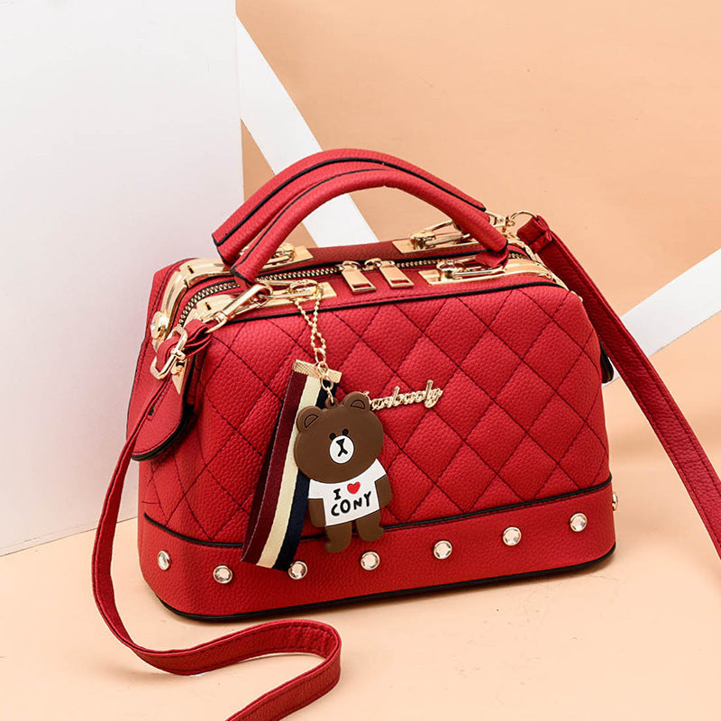 Red quilted messenger bag with gold hardware, studded trim, bear keychain charm