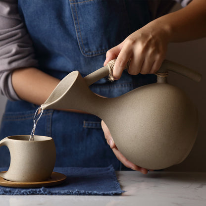 Ceramic water pitcher pouring into cup, with wrapped handle and wooden saucer