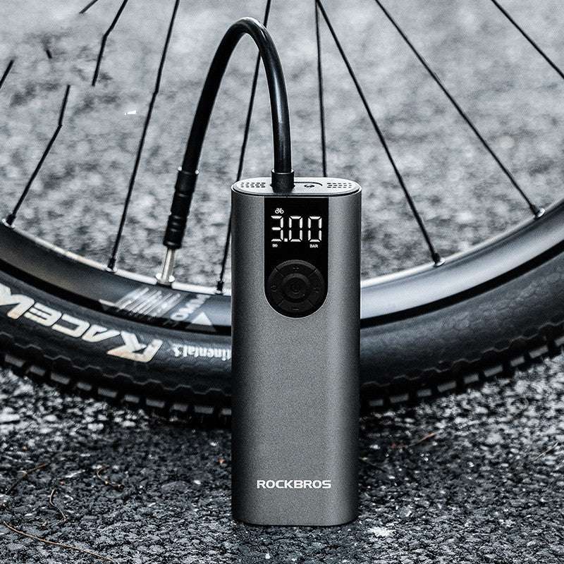 Portable bicycle air pump with digital display next to a bicycle tire on a road.