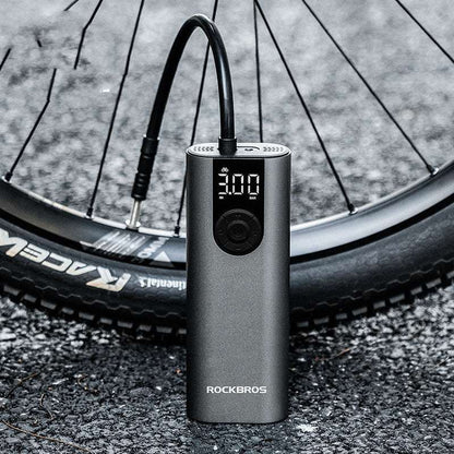 Portable bicycle air pump with digital display next to a bicycle tire on a road.
