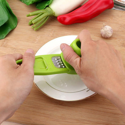 Light green manual garlic masher pressing minced garlic over a bowl