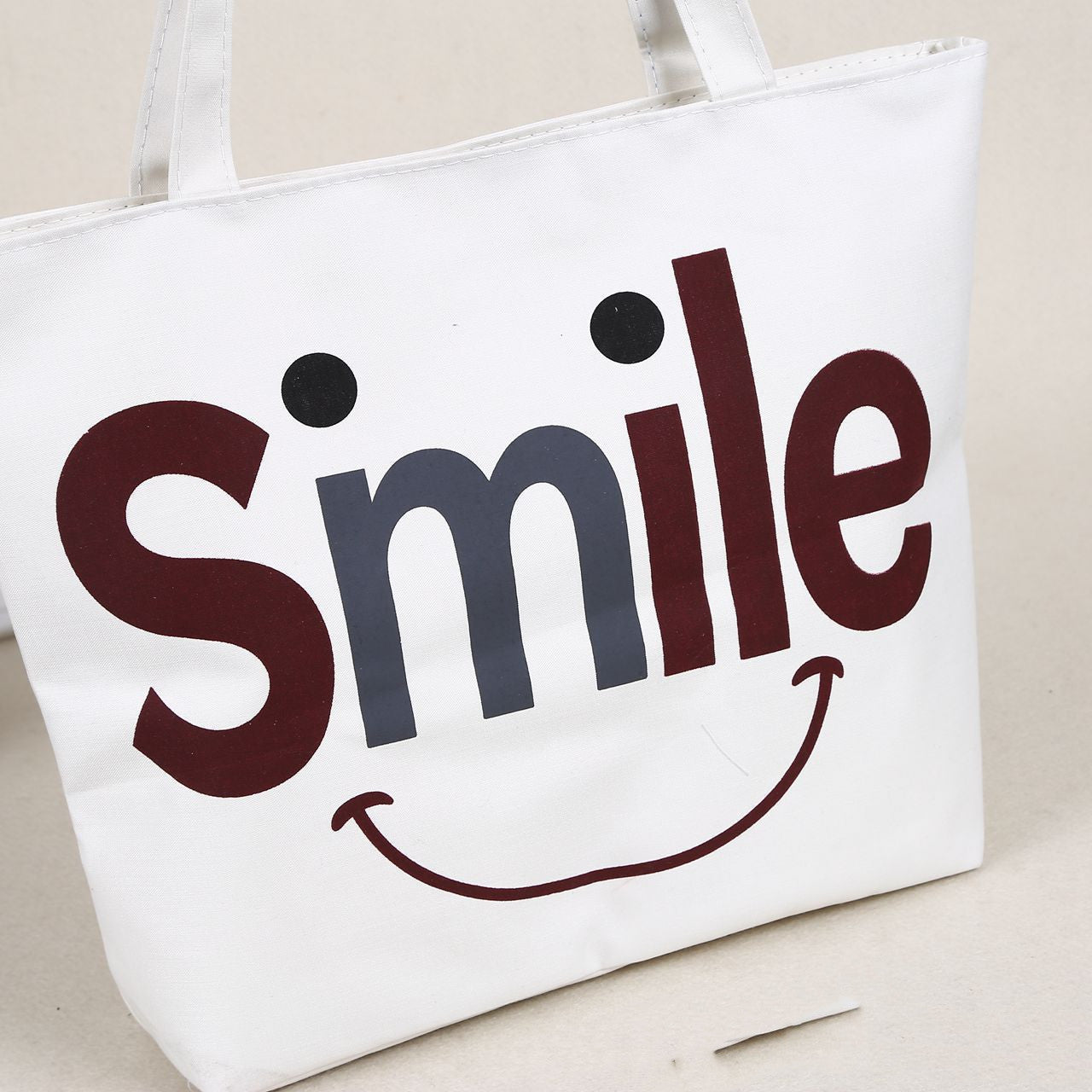 Canvas shoulder bag with white background and large “Smile” face graphic in red and blue