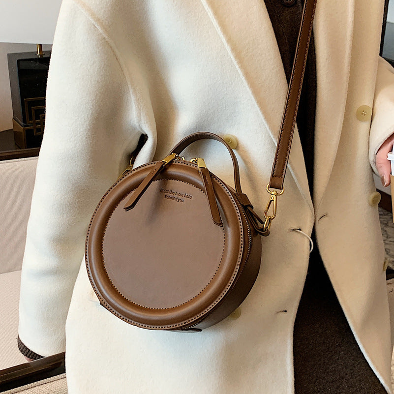 Brown round zip-top crossbody bag with gold-tone hardware and front tassel detail