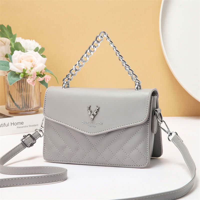 Quilted mini crossbody bag in light gray with silver chain strap and front flap with snap.
