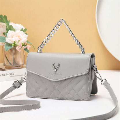 Quilted mini crossbody bag in light gray with silver chain strap and front flap with snap.