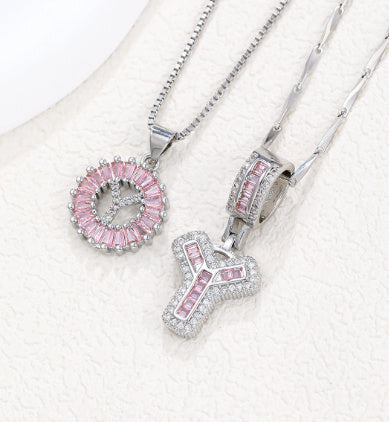 Silver-tone pendant necklace set with pink zircon rosette pendant and bold crossblock letter pendant.