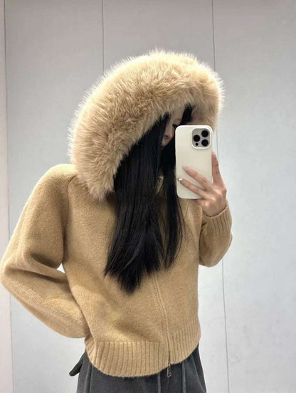Person wearing a beige sweater with a fur-lined hood, taking a mirror selfie.