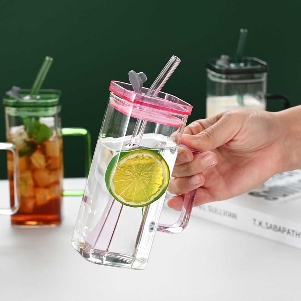 Square glass cup with pink lid and clear straw, held by hand
