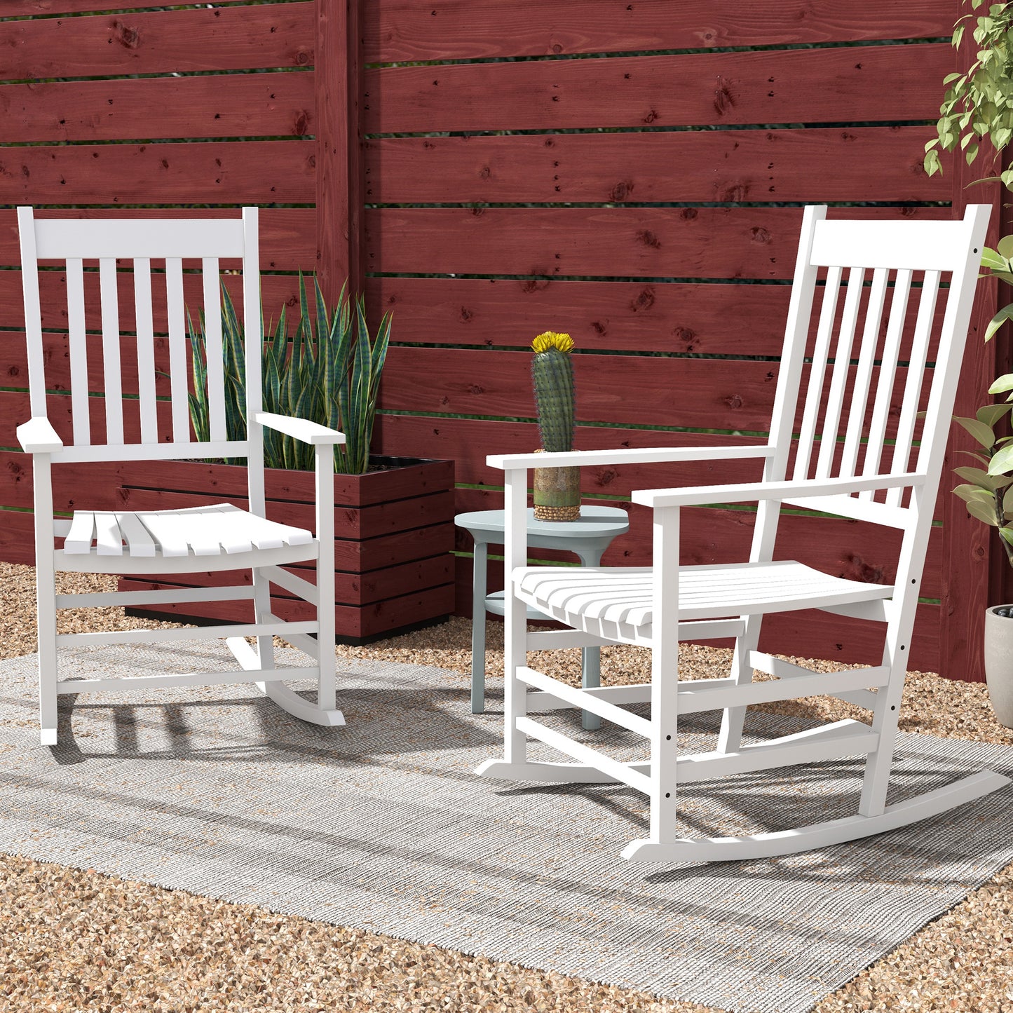 Two white wooden rocking chairs with slatted backs in front of red fence