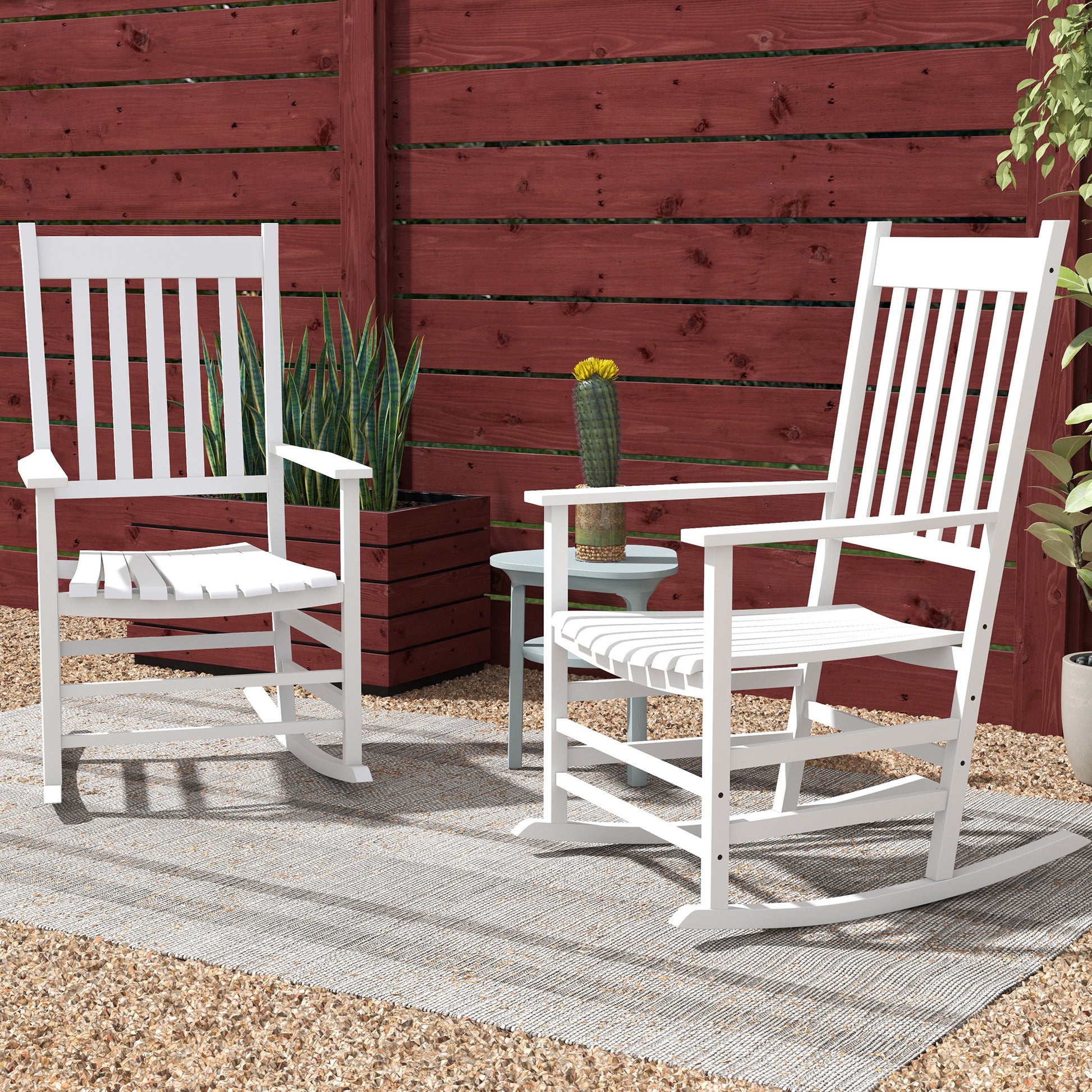 Two white wooden rocking chairs with slatted backs in front of red fence