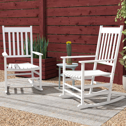Two white wooden rocking chairs with slatted backs in front of red fence
