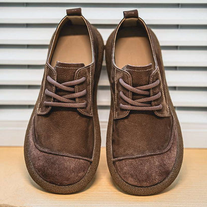 Pair of brown suede shoes on a wooden surface with a striped background