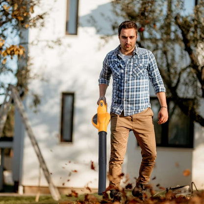 Orange cordless leaf blower held by person for clearing leaves outdoors