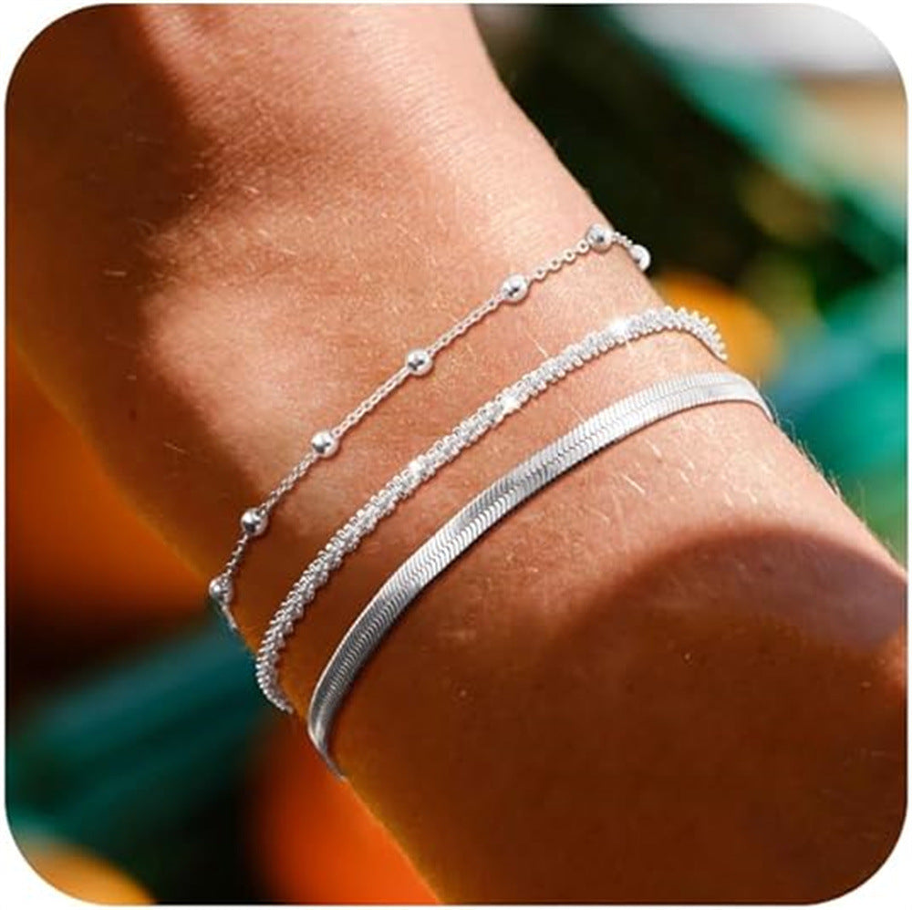 Stacked silver-tone bracelets with curb chain and beaded charm links on wrist